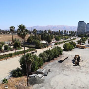 Fotografía de una gran franja de terreno vacío con algunos equipos de construcción y edificios de apartamentos al fondo.