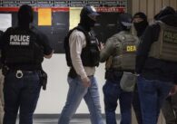 ICE agents wearing masks standing in a hallway