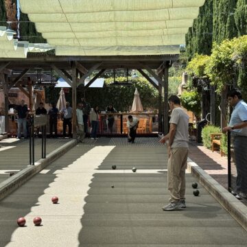 Un grupo de hombres jugando a la petanca en una cancha al aire libre bajo un toldo cubierto.