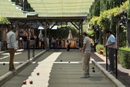 A group of men playing bocce ball on an outdoor court under a covered awning