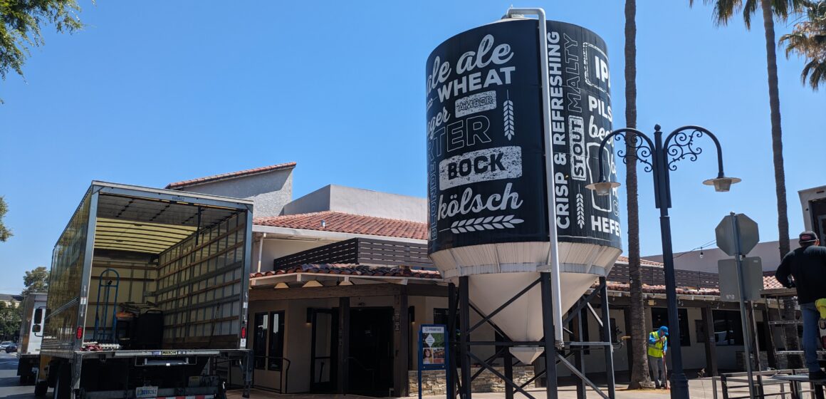 The outside of a restaurant with a moving truck and large water tower with words related to beer on it.