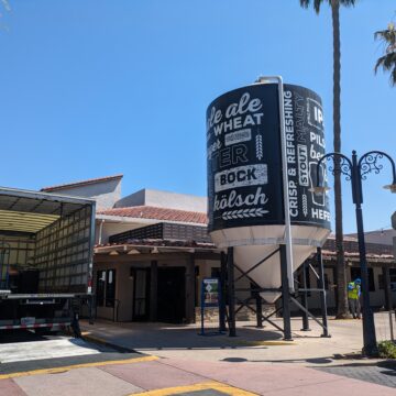 The outside of a restaurant with a moving truck and large water tower with words related to beer on it.