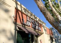 Fotografía de la fachada exterior de la Facultad de Derecho de Lincoln, un edificio de una sola planta de color beige y ladrillo con toldos oscuros sobre las ventanas.