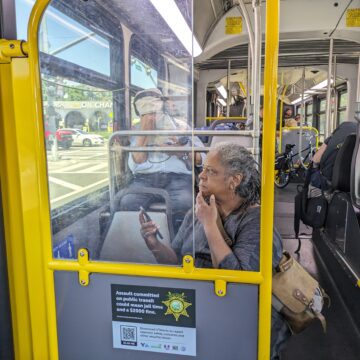 Una mujer mayor se sienta en un autobús público con su teléfono en la mano y un bolso sobre el hombro mirando por la ventana.