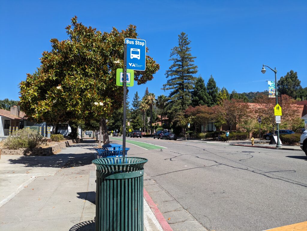 A pole in between two trash cans with a blue sign attached that reads "Bus Stop"