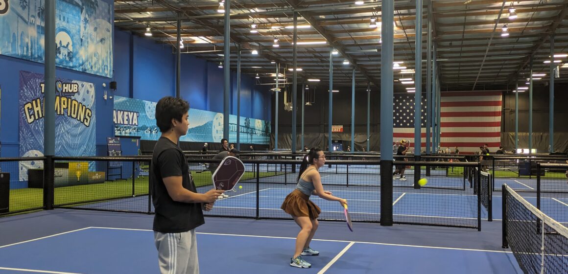 Two young people play pickleball in an indoor court