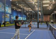 Two young people play pickleball in an indoor court