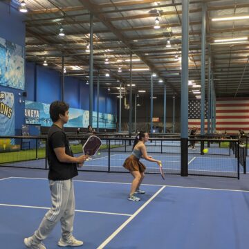 Two young people play pickleball in an indoor court