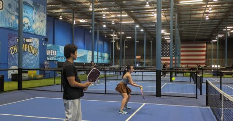 Two young people play pickleball in an indoor court