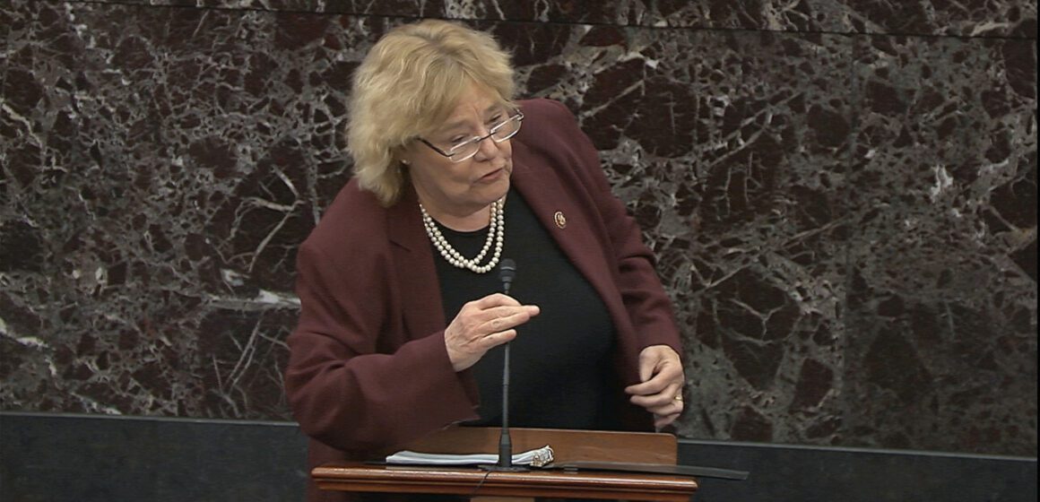 A woman in a blazer speaks into a microphone at a podium