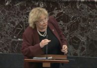 A woman in a blazer speaks into a microphone at a podium