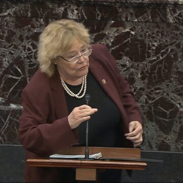 A woman in a blazer speaks into a microphone at a podium