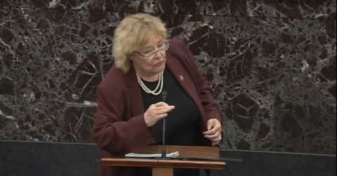 A woman in a blazer speaks into a microphone at a podium