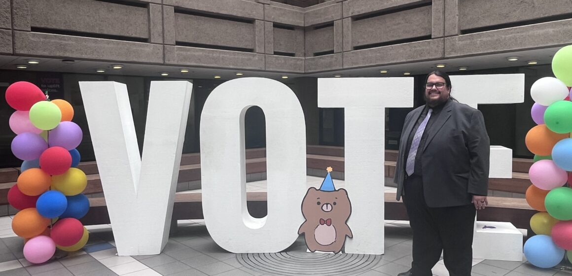 ROV SITDOWN A man in a suit stands in front of large letters reading VOTE
