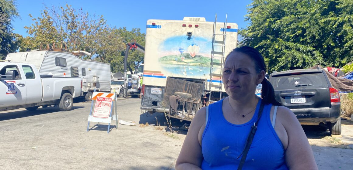 A woman stands in front of RVs and other vehicles in a homeless camp in San Jose, California