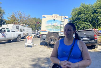 A woman stands in front of RVs and other vehicles in a homeless camp in San Jose, California