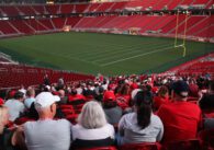 Photo of dozens of people wearing red, white, and gold, sitting in one section of Levi's Stadium, with the empty field and other empty sections visible in the background