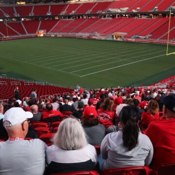 Photo of dozens of people wearing red, white, and gold, sitting in one section of Levi's Stadium, with the empty field and other empty sections visible in the background