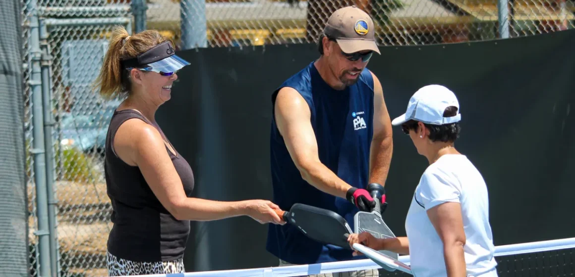 Three people bump rackets on a pickleball court