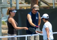 Three people bump rackets on a pickleball court