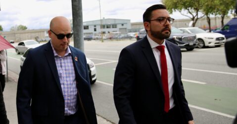 A man in a blazer walks on the sidewalk next to a man in a suit and tie