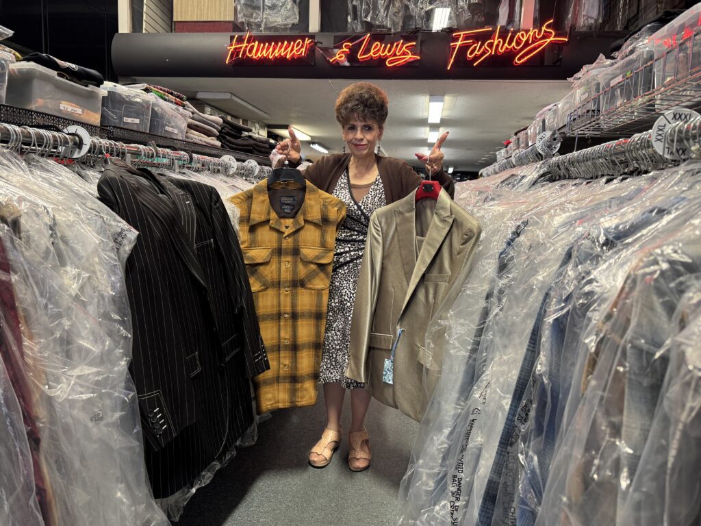 A woman standing in a clothing store holding a man's shirt and jacket