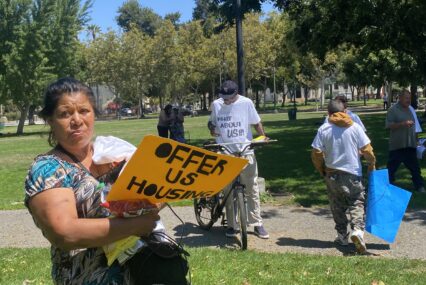 People holding protest signs in a park in downtown San Jose, California
