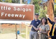 Una mujer y dos hombres de pie frente a una señal de autopista.
