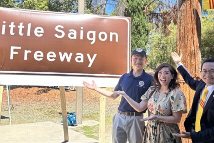 A woman and two men standing in front of a freeway sign