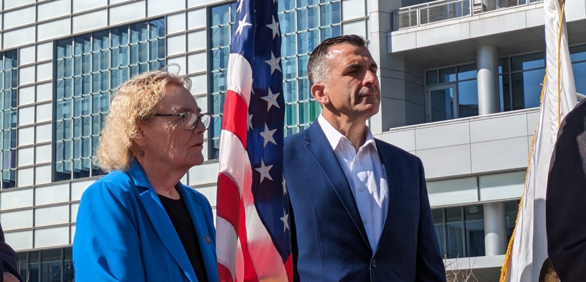 An older woman and middle-aged man stand next to an American flag