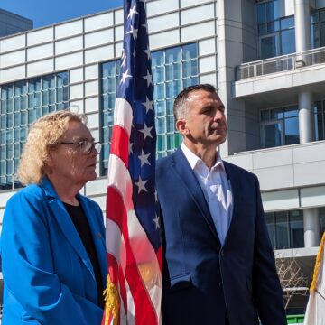 An older woman and middle-aged man stand next to an American flag