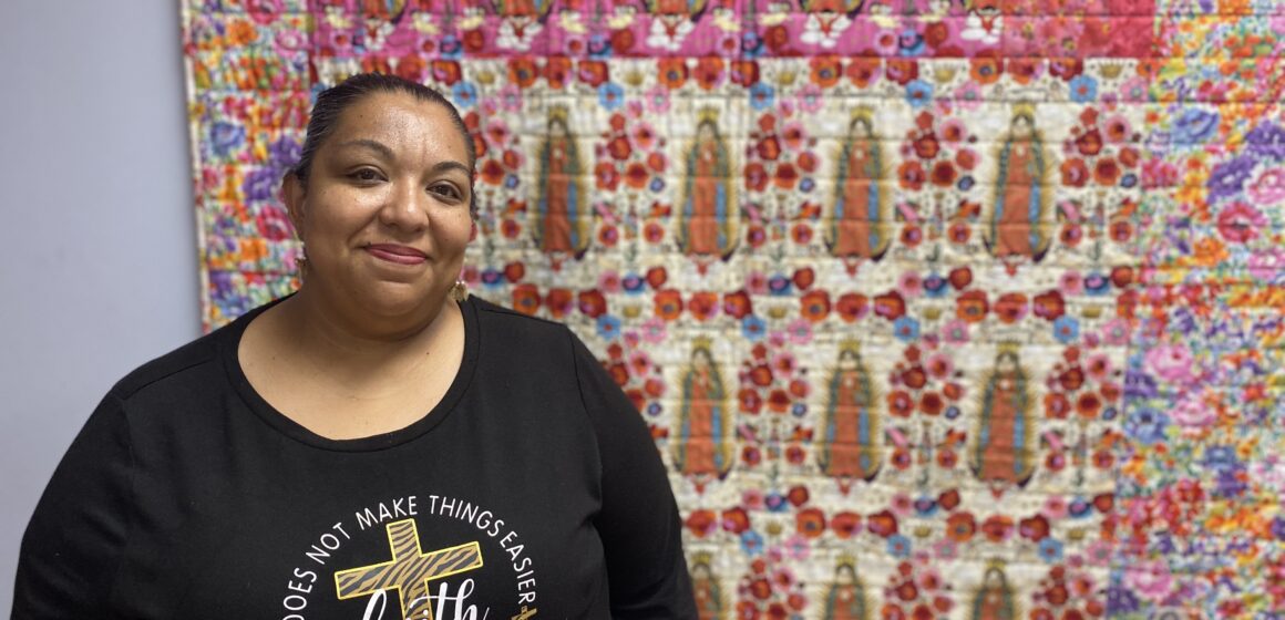 A woman stands in front of a quilt