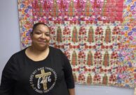 A woman stands in front of a quilt