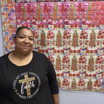 A woman stands in front of a quilt