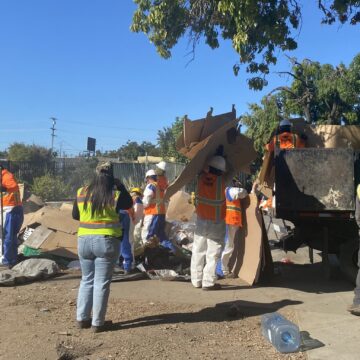 Columbus Park Decommission People in reflective vests throw trash from a homeless encampment into a dumpster