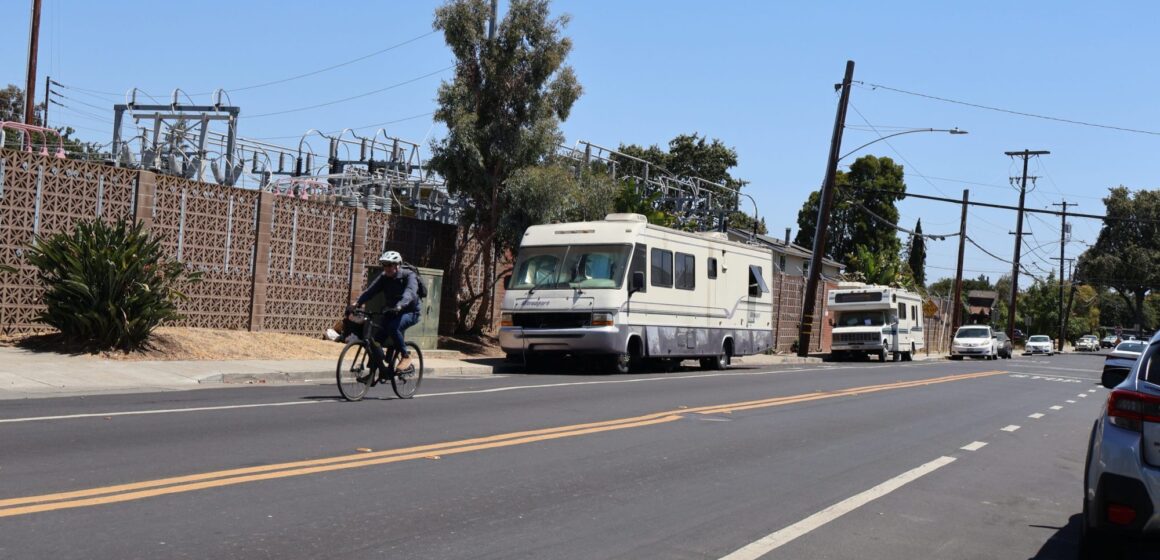 A cyclist rides past two lived-in RVs on a street in Palo Alto, California
