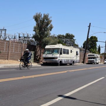 A cyclist rides past two lived-in RVs on a street in Palo Alto, California