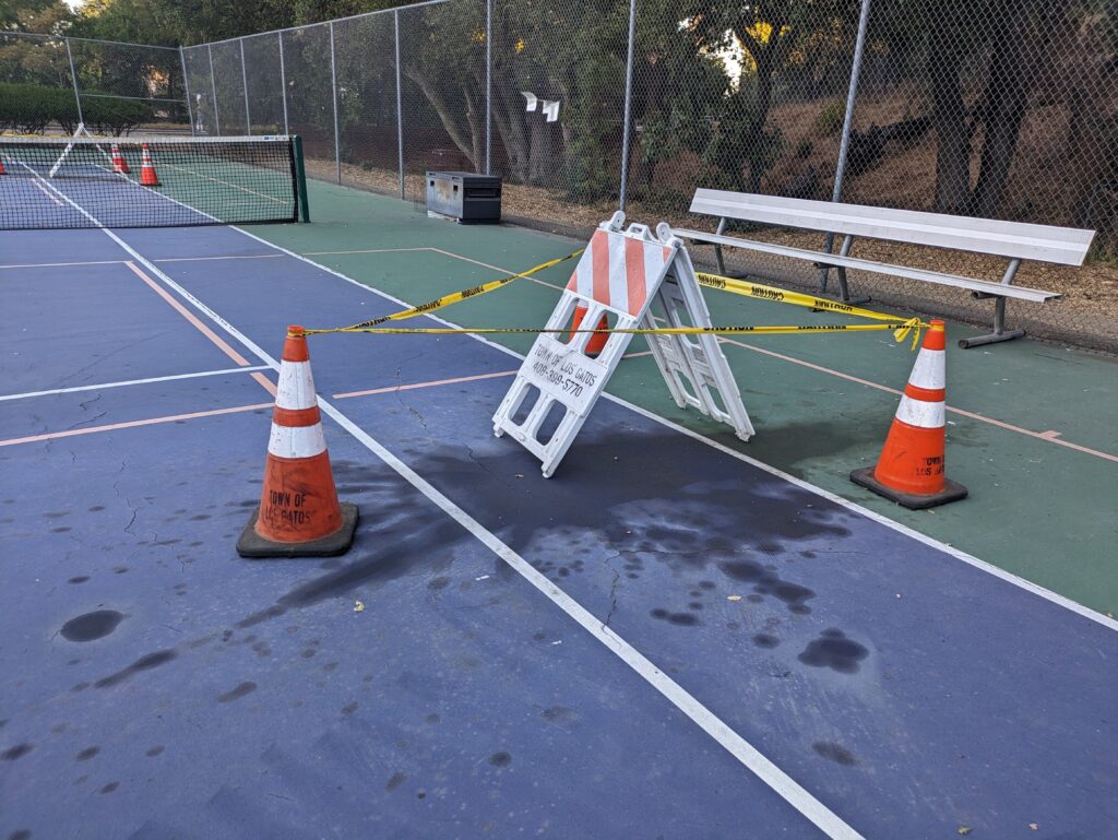 Orange cones and caution tape block off an oil spill on a pickleball court