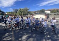 Elementary school students sit on bikes in a parking lot