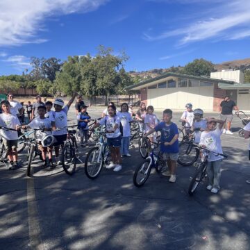 Elementary school students sit on bikes in a parking lot