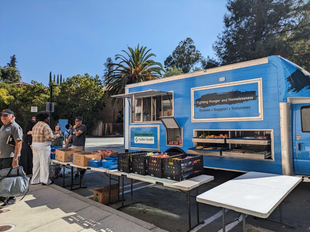 A blue van is parked next to tables of food in boxes
