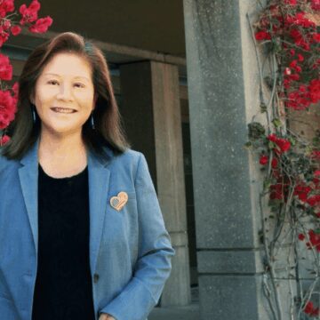 Hung Wei An older Taiwanese woman stands smiling in front of a trellis with flowers
