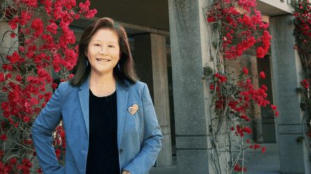 An older Taiwanese woman stands smiling in front of a trellis with flowers