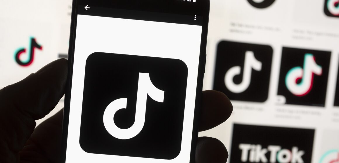 A hand holding a phone displaying the tiktok logo, with other tiktok logos in the background
