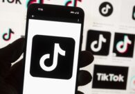 A hand holding a phone displaying the tiktok logo, with other tiktok logos in the background