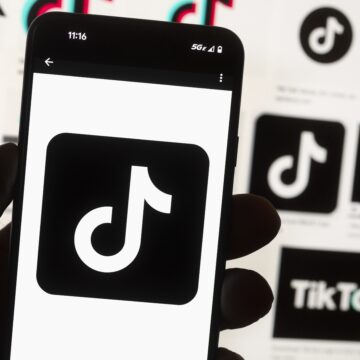 A hand holding a phone displaying the tiktok logo, with other tiktok logos in the background