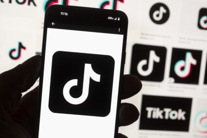 A hand holding a phone displaying the tiktok logo, with other tiktok logos in the background