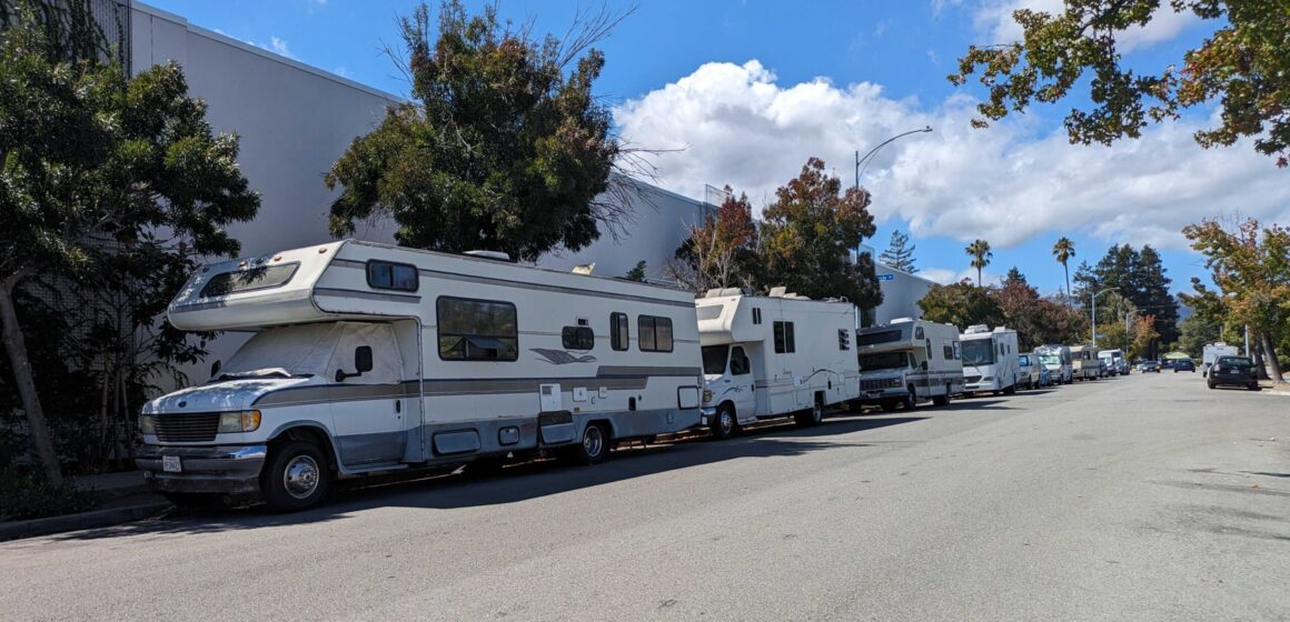 Four RVs parked in a row on a public residential street.