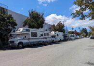 Four RVs parked in a row on a public residential street.