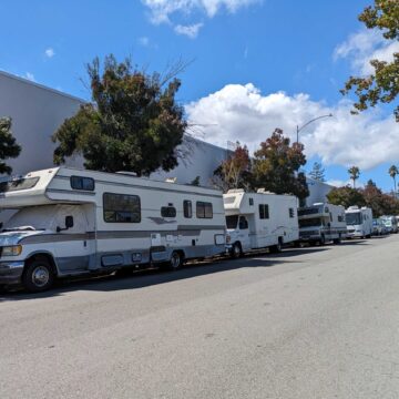Four RVs parked in a row on a public residential street.